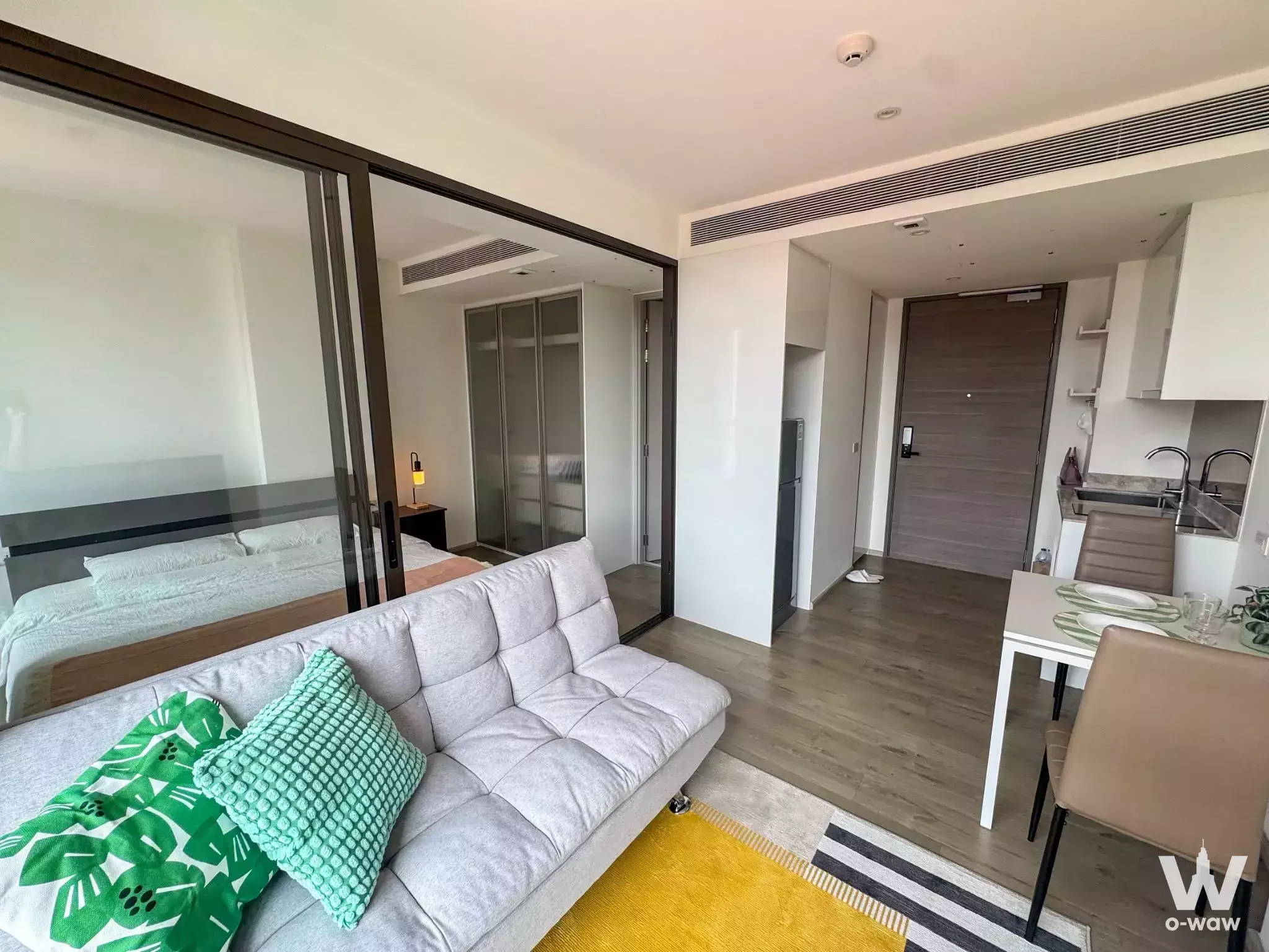 Modern 1-bed condo for rent in Fynn Asoke with open-plan living, light wood floors, and city views through glass doors