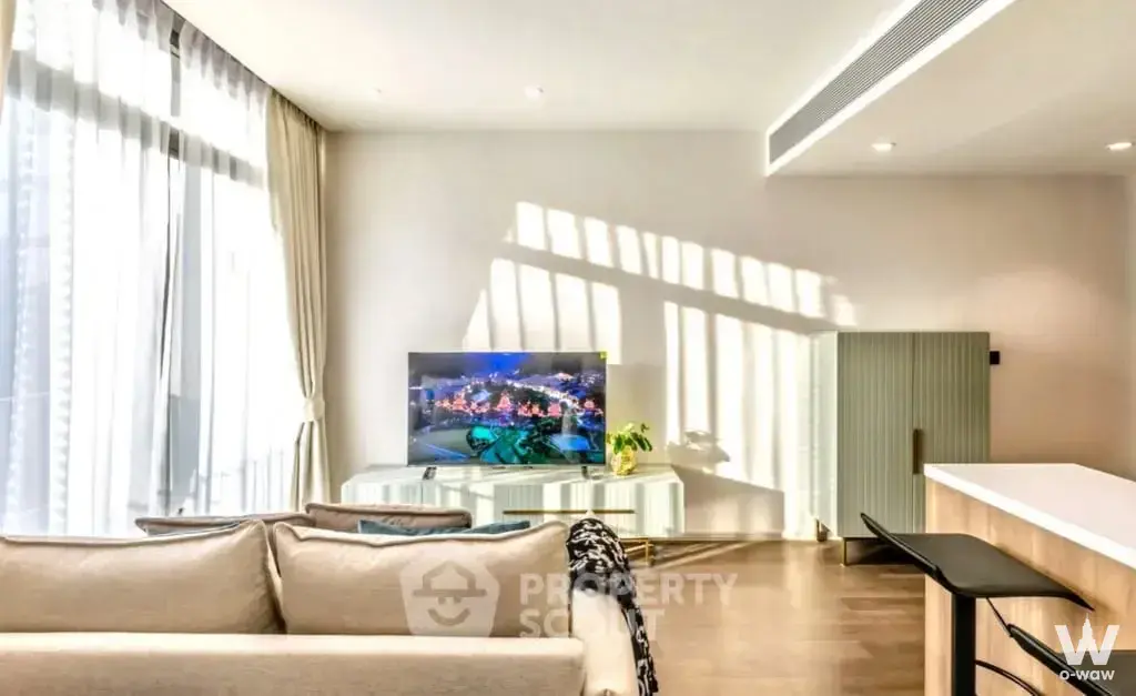Bright living room in 2-bed MUNIQ Sukhumvit 23 condo with wood floors, beige sofa, and floor-to-ceiling windows