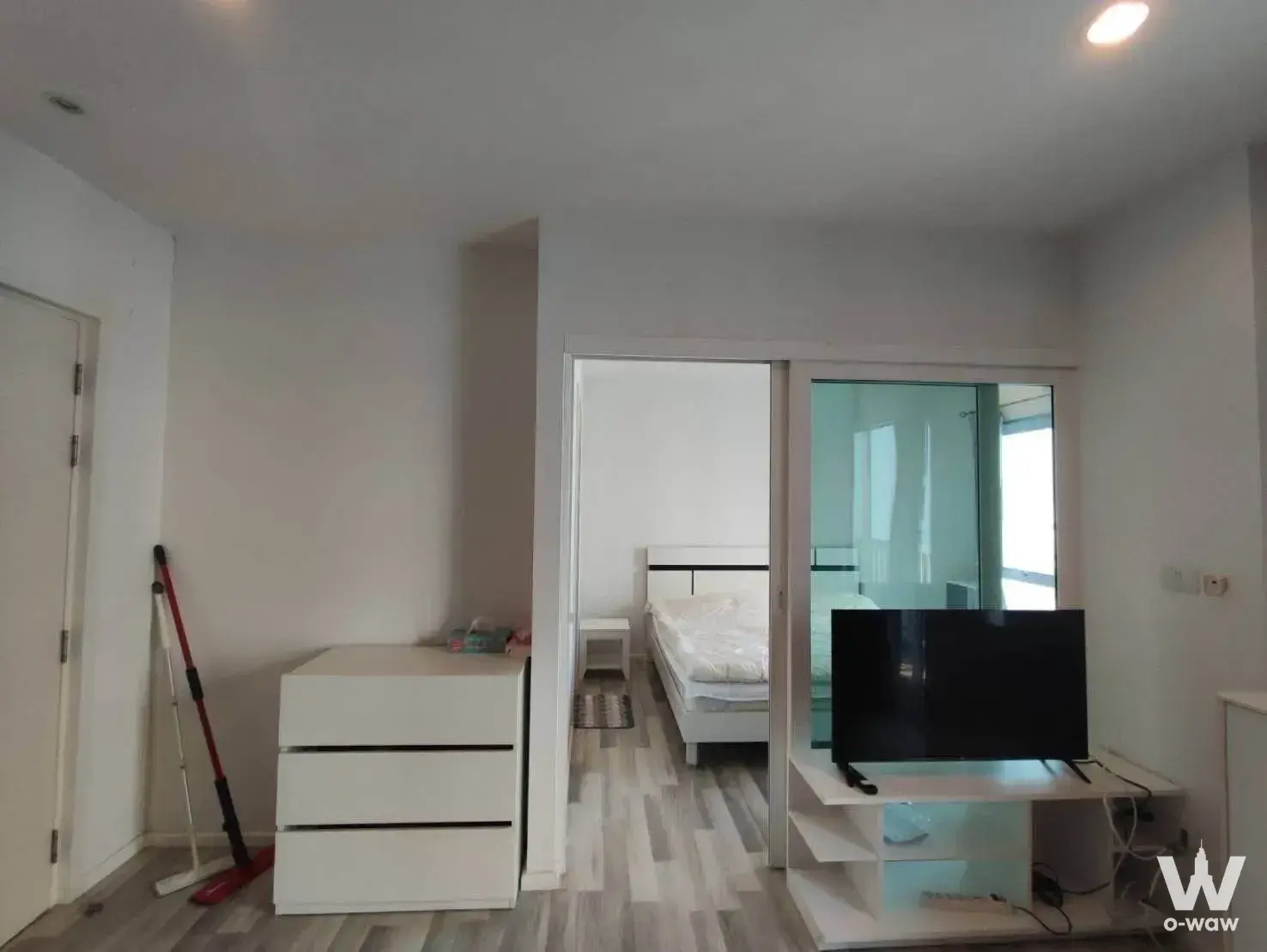Bright 1-bed condo bedroom for rent in The Key Cheangwattana with white walls, grey flooring, TV console, and frosted glass
