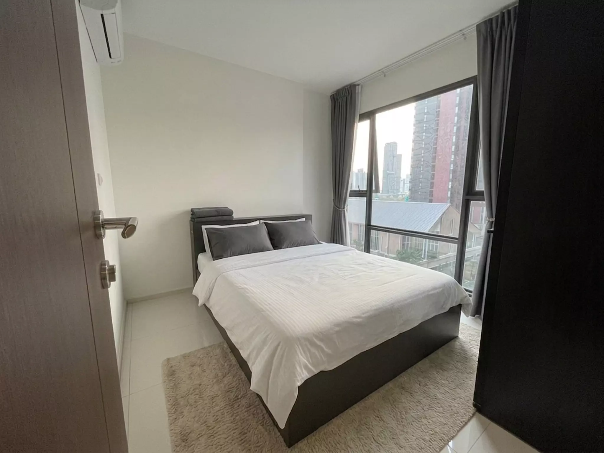 Modern bedroom in 2-bed Rhythm Asoke condo with queen bed, shag rug, and floor-to-ceiling windows overlooking Bangkok skyline
