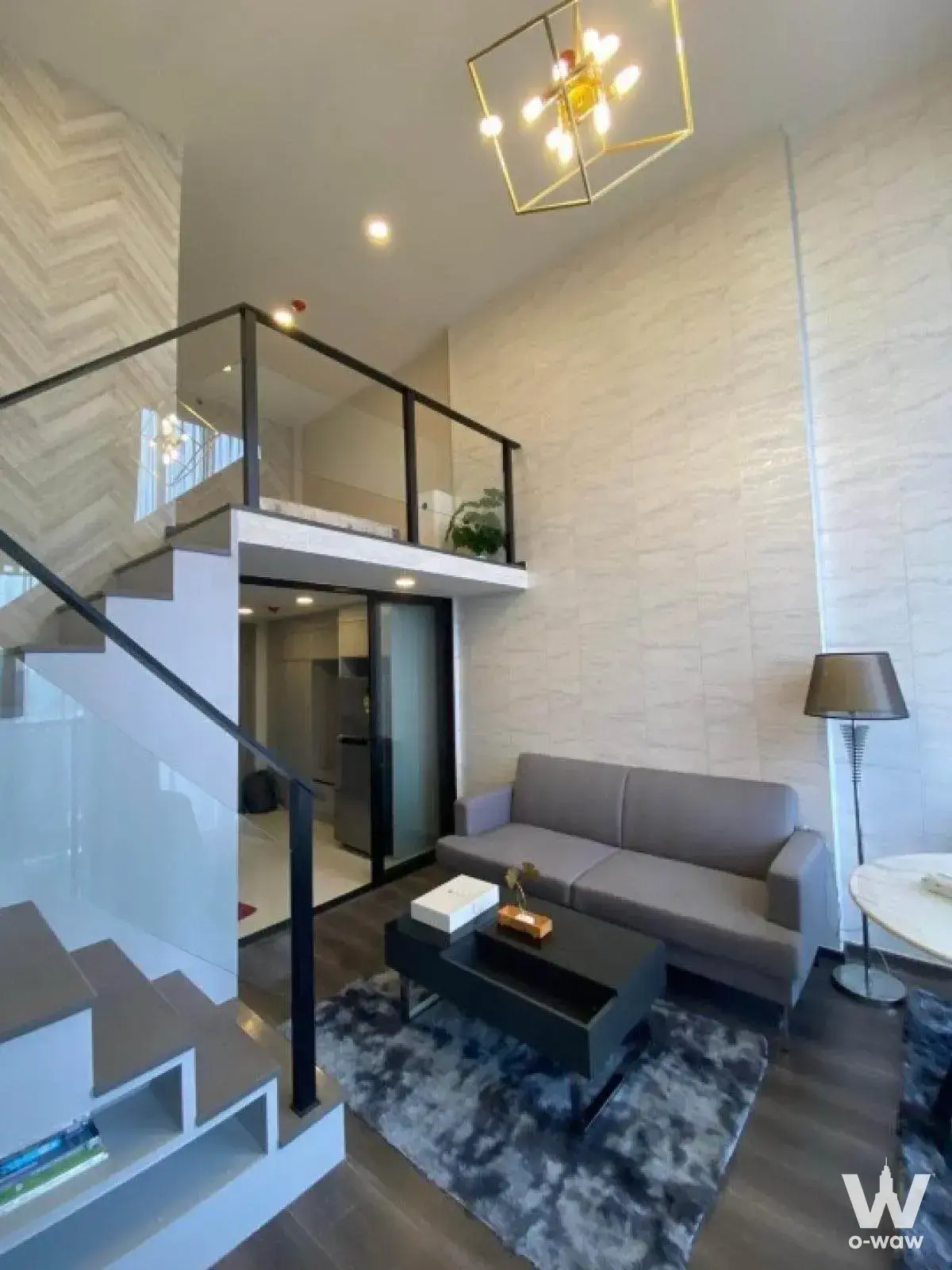 Duplex living area in KnightsBridge Space Ratchayothin with double-height ceilings and a modern open staircase