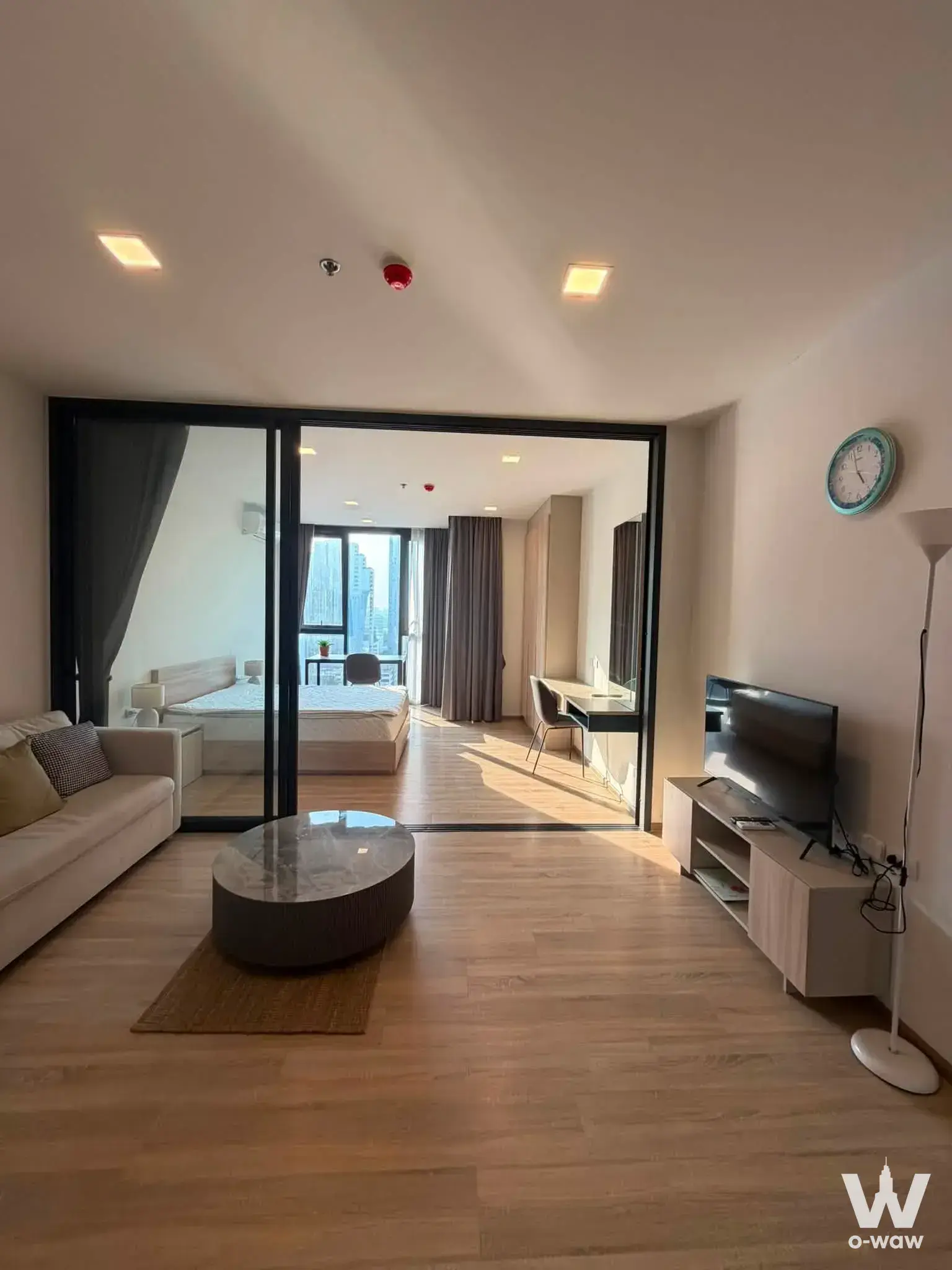 Modern 1-bed condo for rent in XT Phayathai with black-framed glass doors, beige sofa, and city views