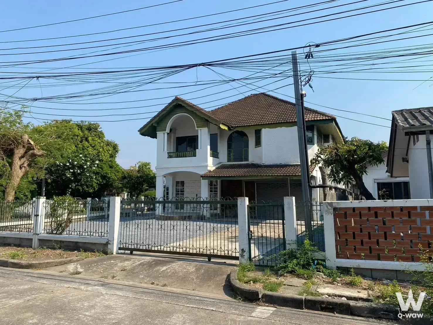 Two-story white stucco house for rent in Sammakon Village with arched balcony and metal garage door behind iron fence