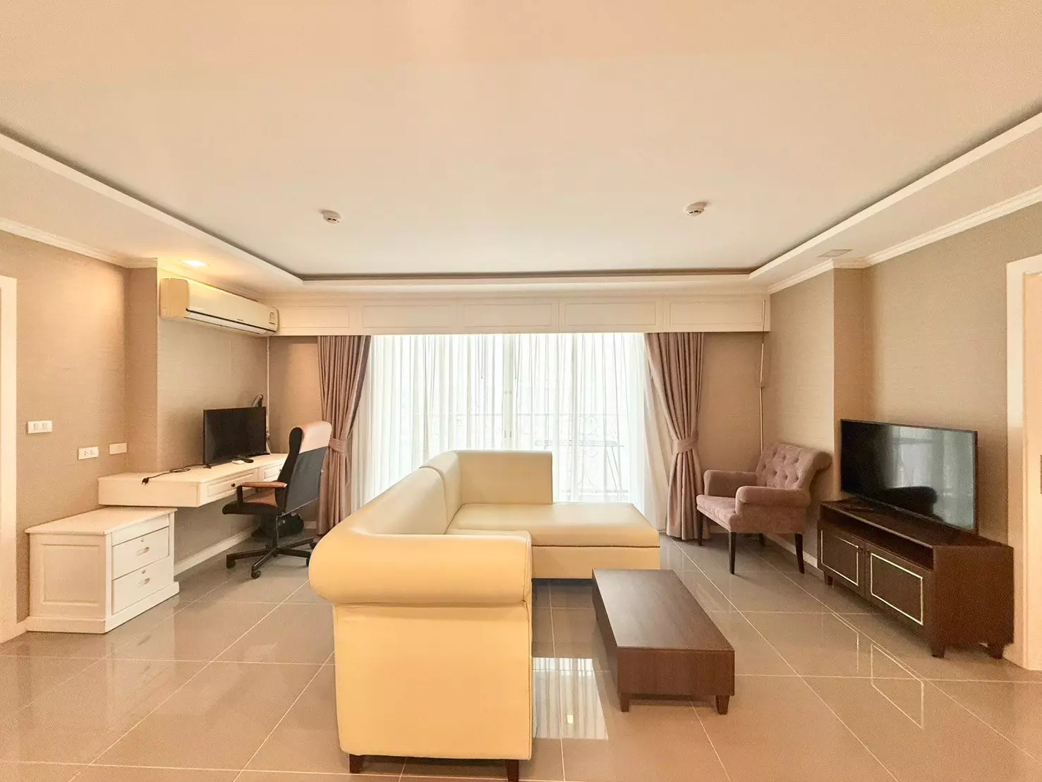 Modern living room with cream sectional sofa and workspace in 2-bed condo for rent at The Orient Resort & Spa Bangkok