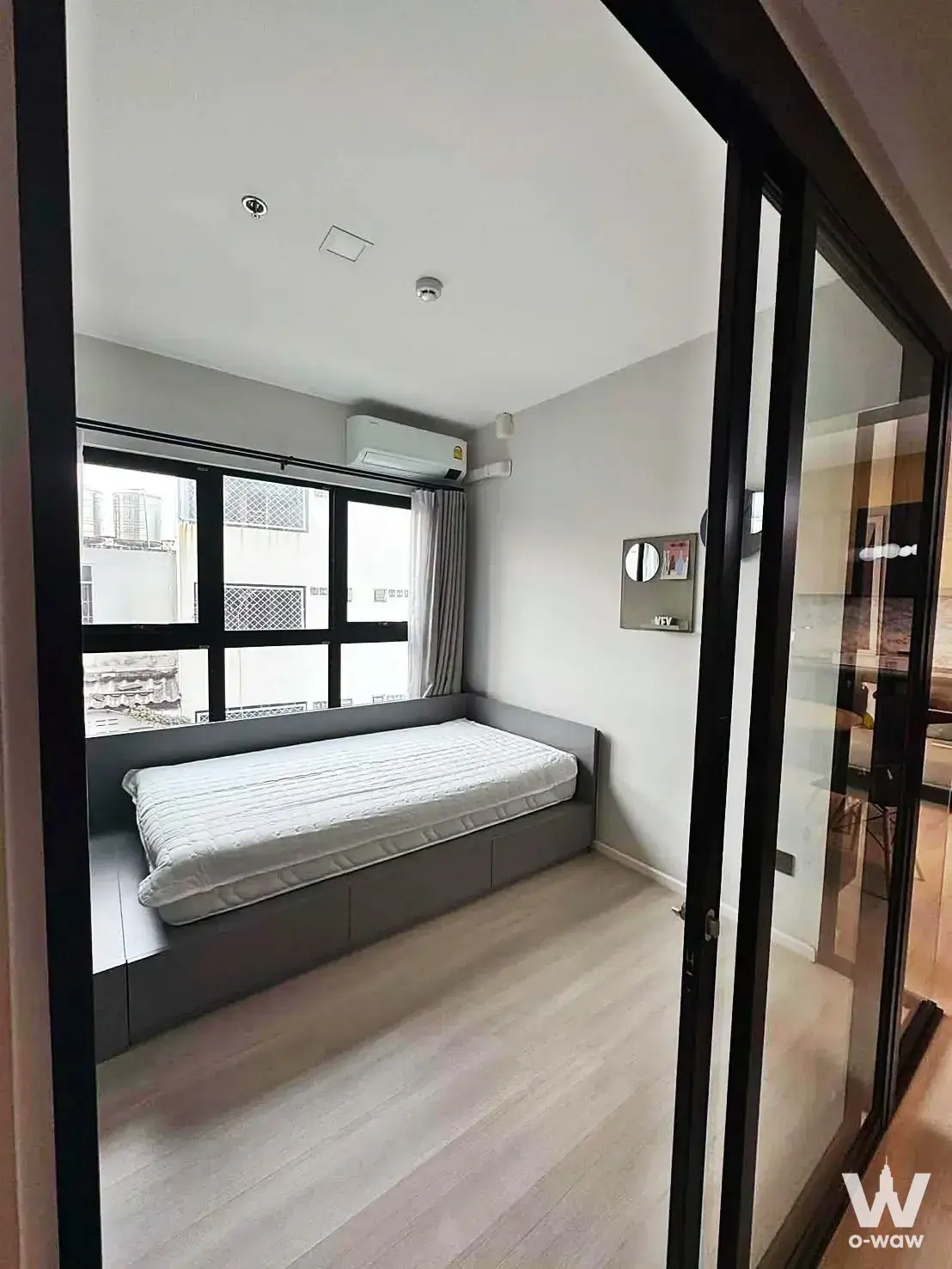 Modern bedroom in 2-bed condo for rent at The Key MRT Phetkasem 48 featuring built-in window seat bed and black-framed glass