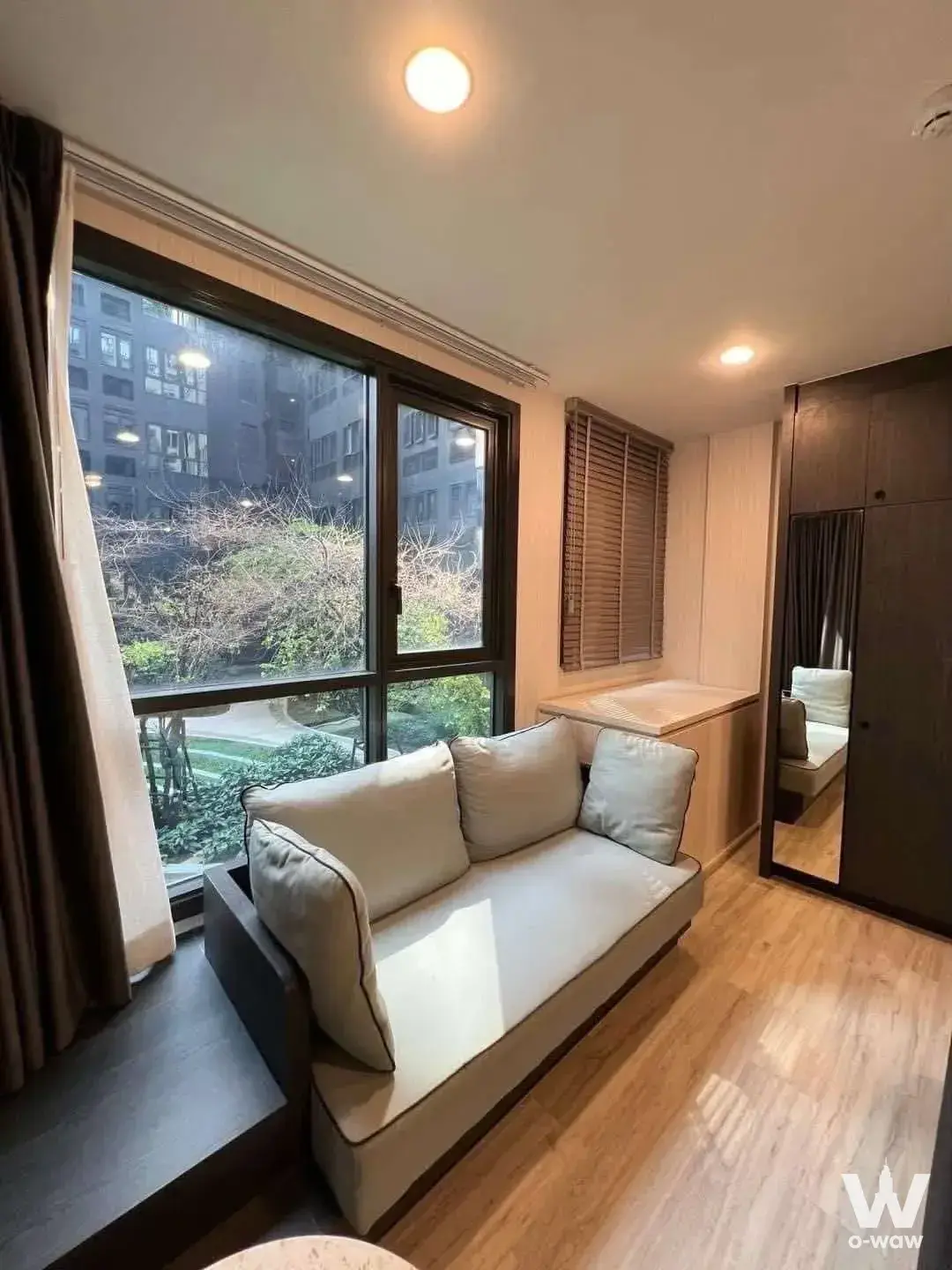 Modern 1-bed condo bedroom in XT Huai Khwang with large window, beige sofa bed, and built-in wardrobe