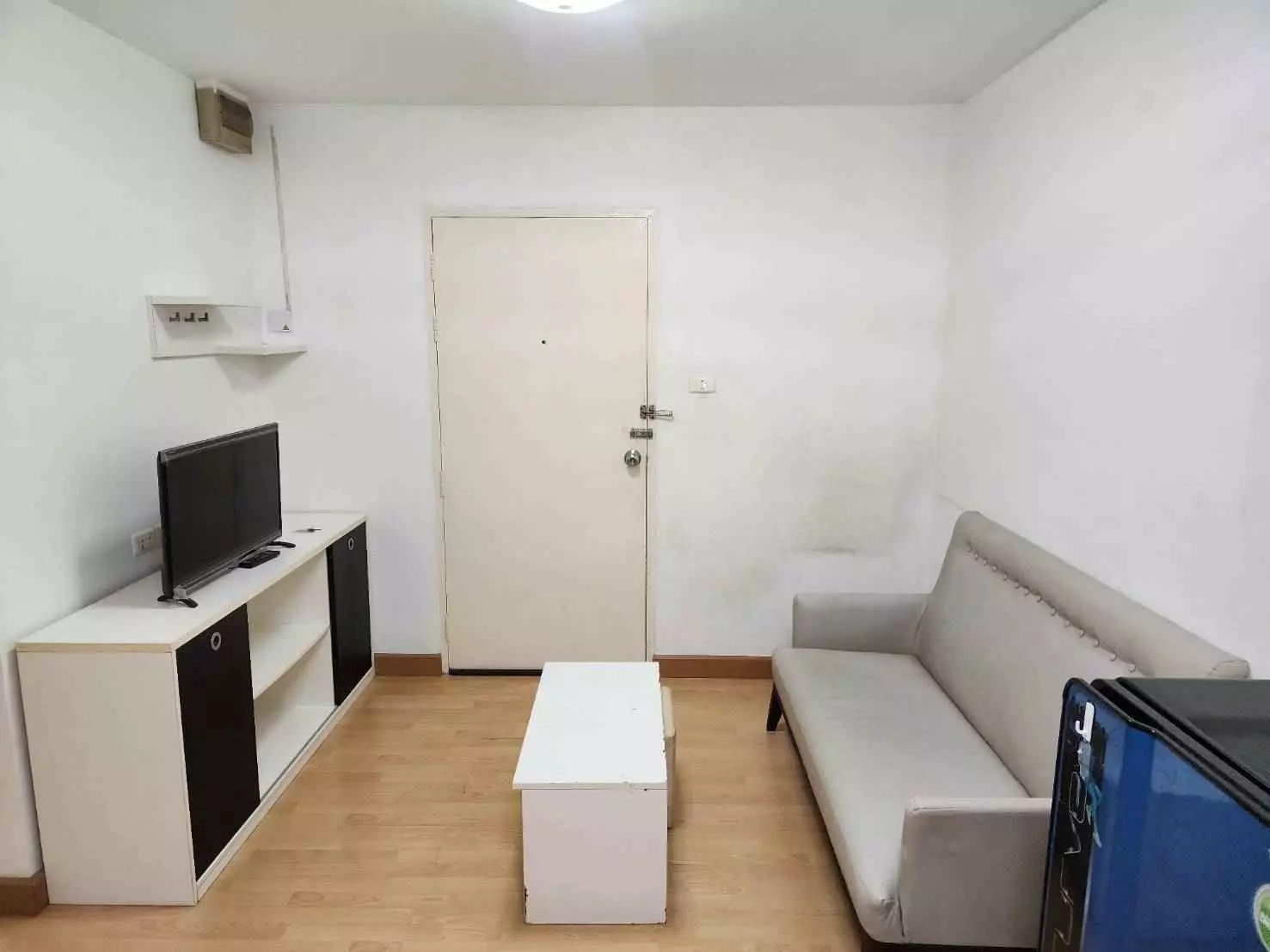 Minimalist living room with grey sofa, white media console, and wood flooring in 1-bed condo for rent at Smart Condo RAMA II