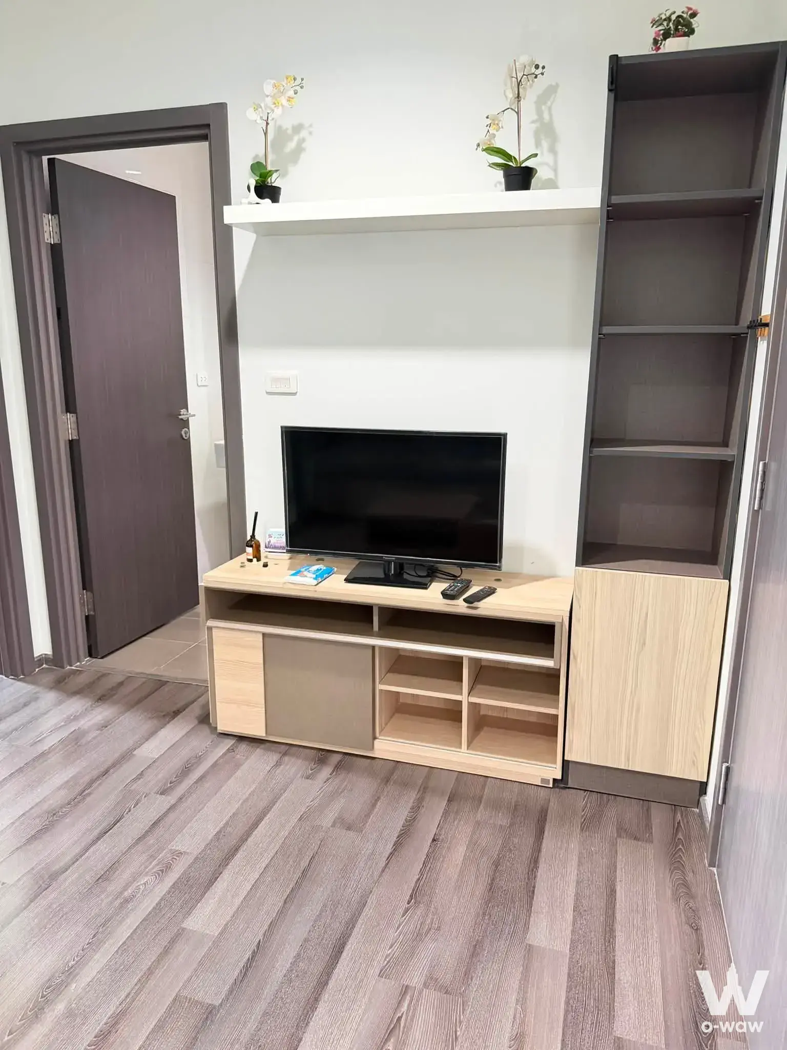 Modern living room with oak TV console, orchids, and grey bookshelf in 1-bed condo for rent at The Park Condominium Bangkok