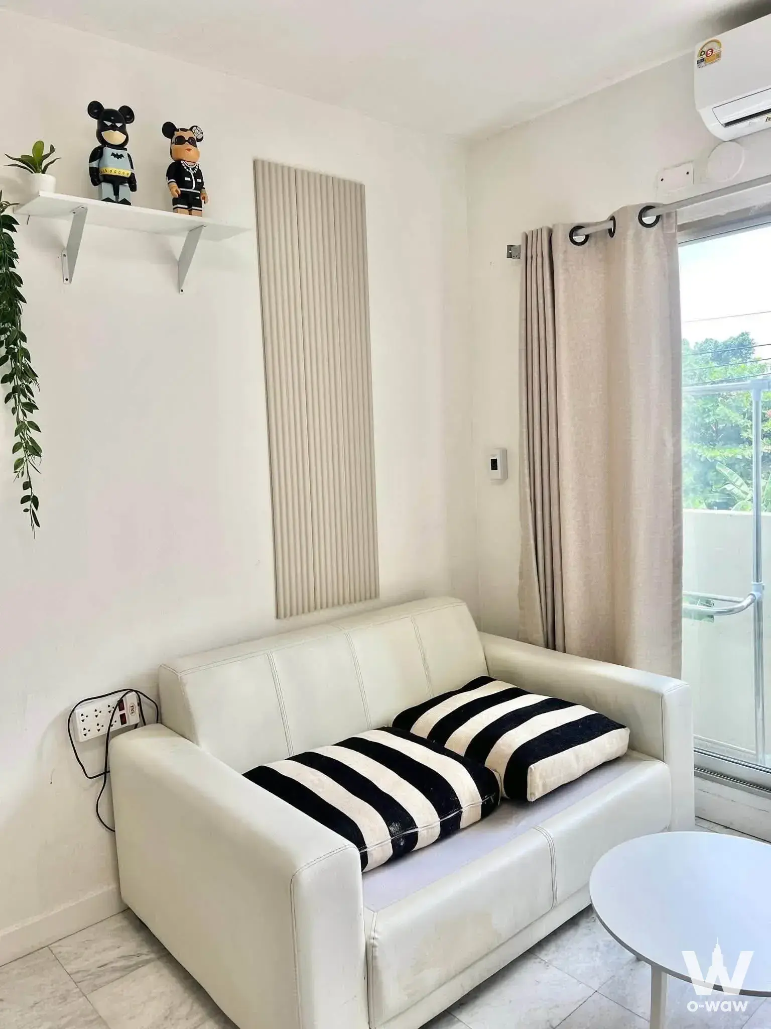 Modern living room with white sofa, striped pillows, and bearbrick figurines on a floating shelf