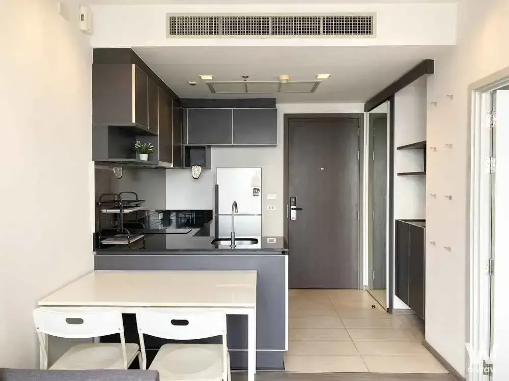 Modern 1-bed condo kitchen in Nye by Sansiri with dark grey cabinets, black countertops, and white dining set