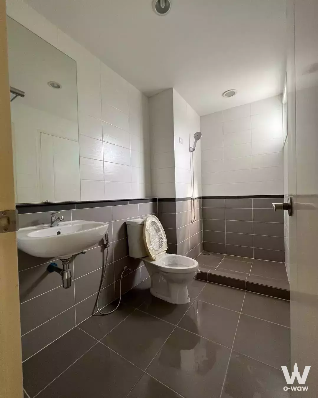Modern bathroom with two-tone grey and white tiles, wall-mounted sink, and open shower in 3-bed condo for sale in Suanluang