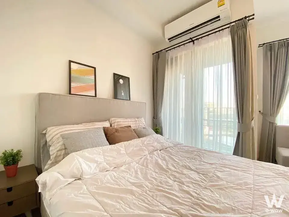 Modern bedroom with queen bed, sheer curtains, and floor-to-ceiling windows overlooking a balcony in bright daylight