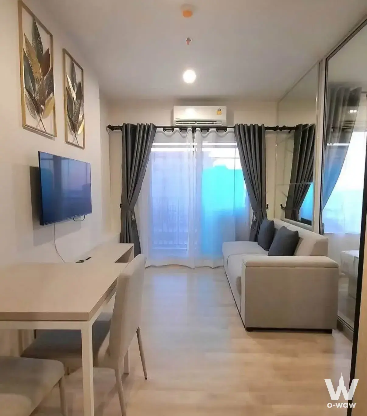 Furnished living area in Niche MONO Ramkhamhaeng with beige sofa and large window with sheer curtains
