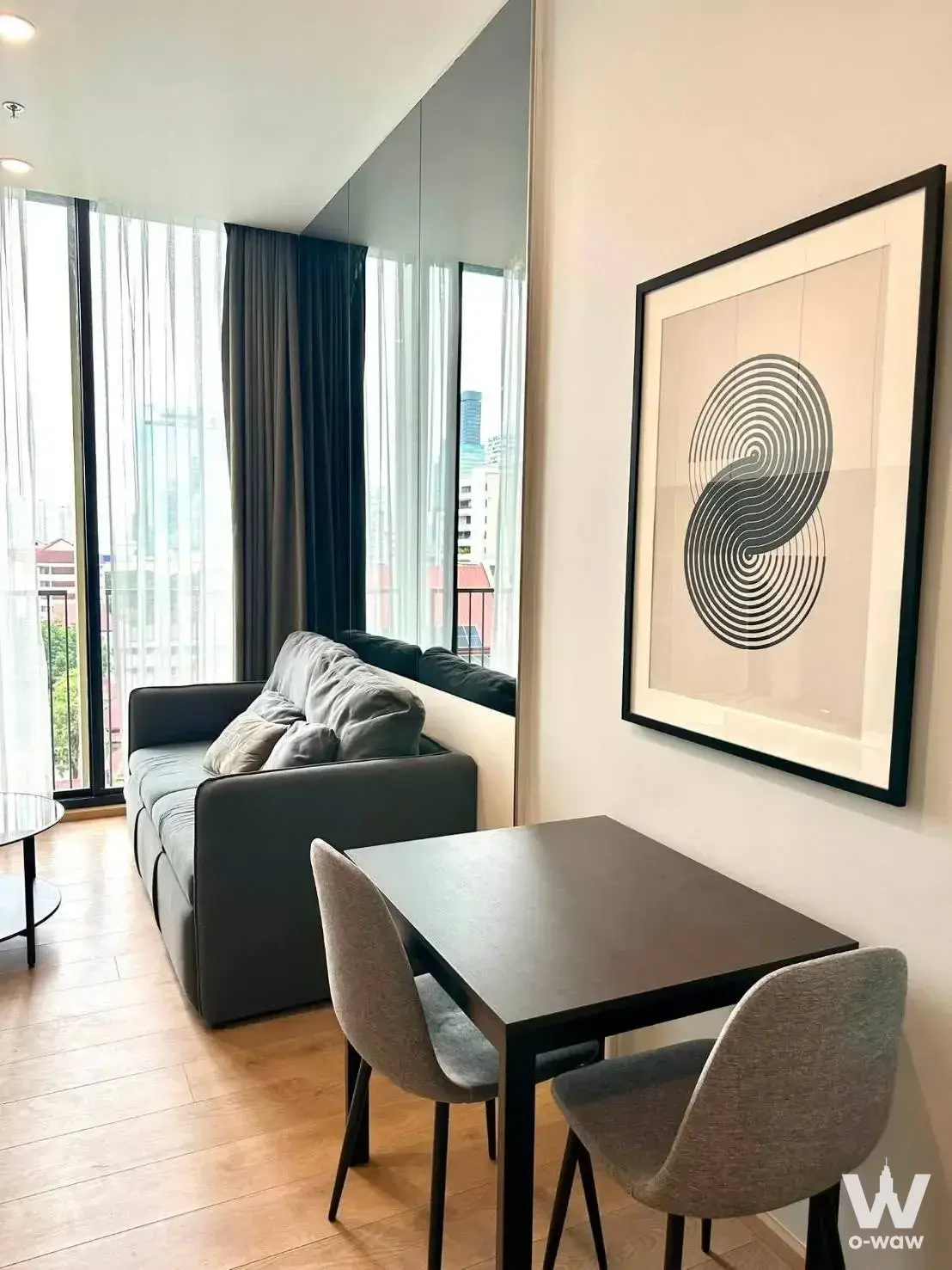 Modern living room in Keyne by Sansiri 1-bed condo with grey sofa, mirrored wall, and city views