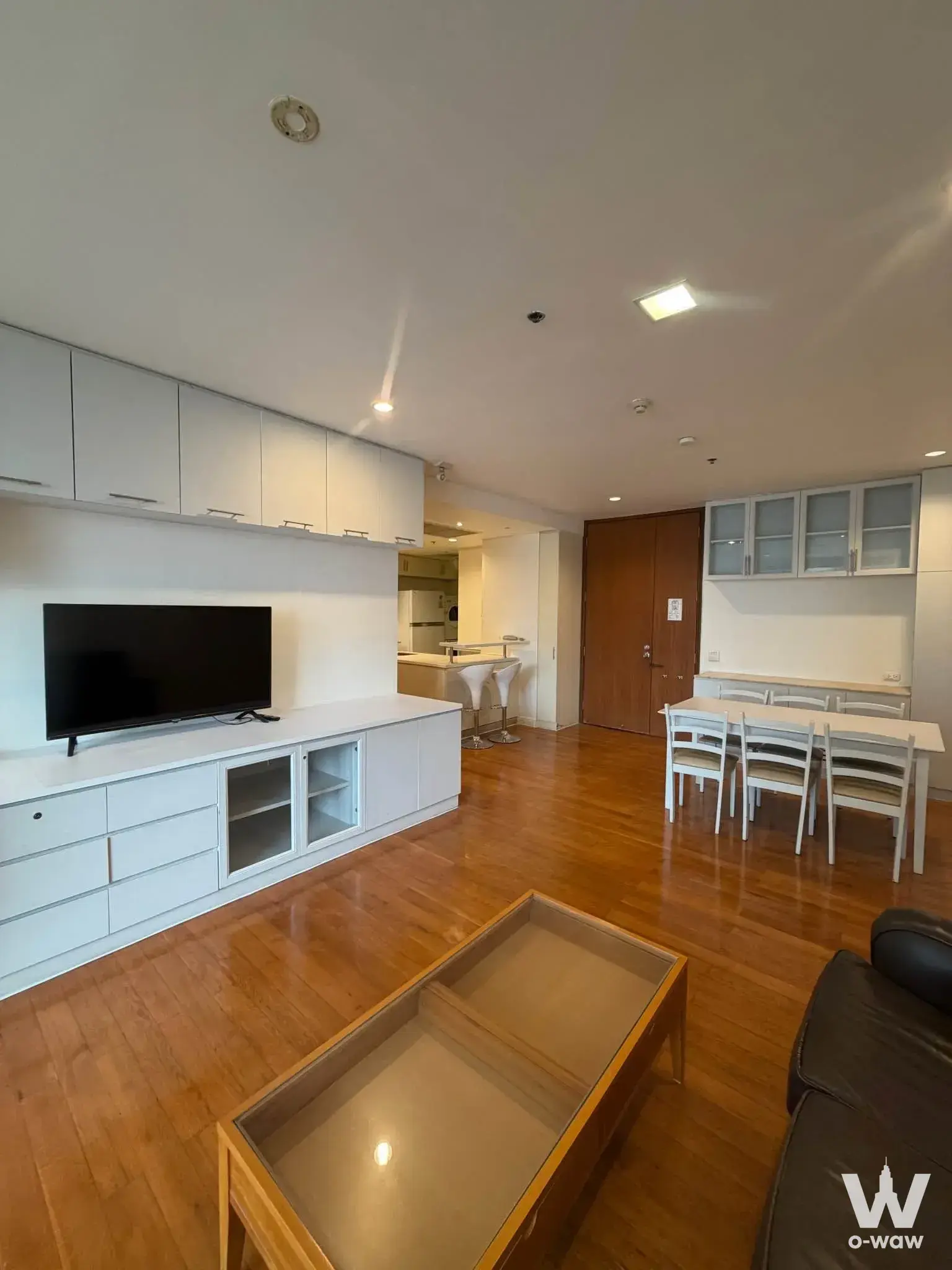 Open-plan living area in a Royal Saladaeng 3-bed condo featuring hardwood floors, white cabinetry, and a dining zone