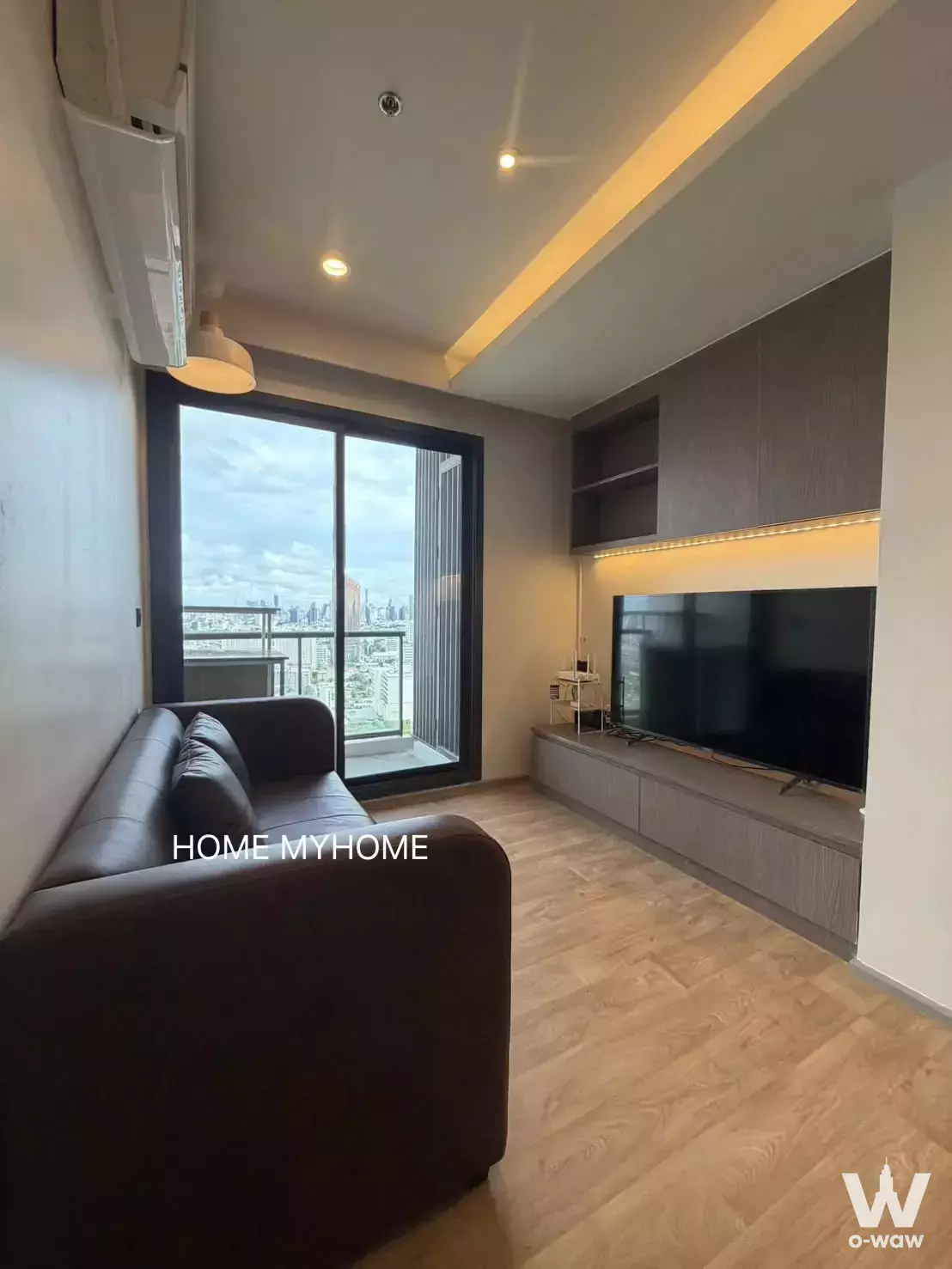 Modern living room in 2-bed M Jatujak condo with leather sofa, LED TV unit, and balcony city views
