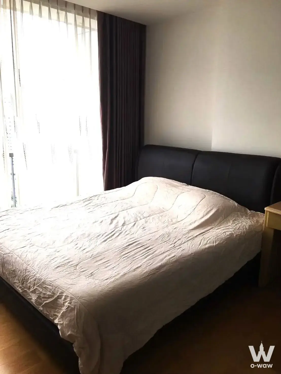 Bedroom in a 1-bed Noble Revo Silom condo with a black leather headboard, white duvet and large curtained window