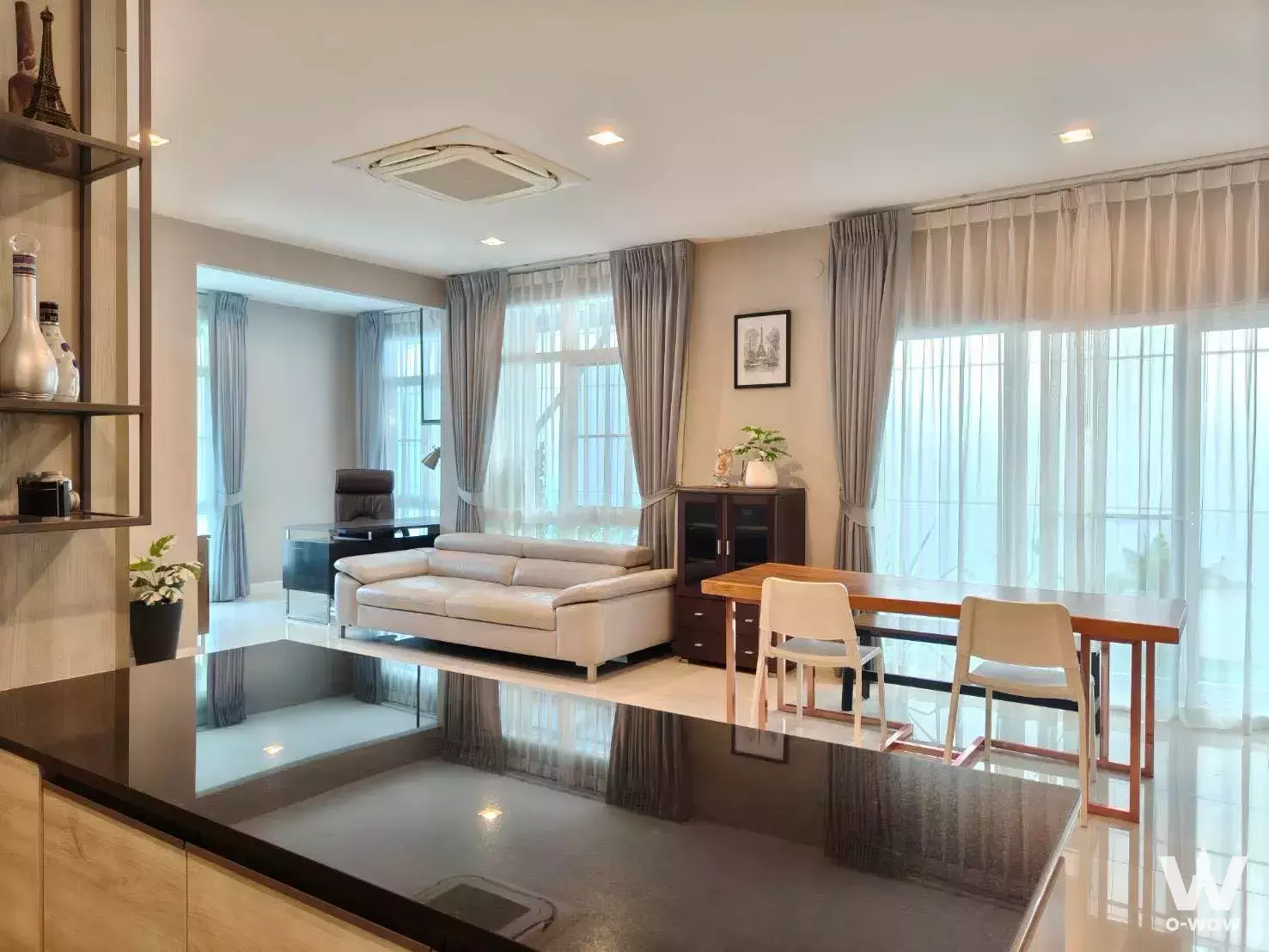 Modern open-plan living and dining area with beige sofa, wooden table, and floor-to-ceiling windows in 4-bed house for rent