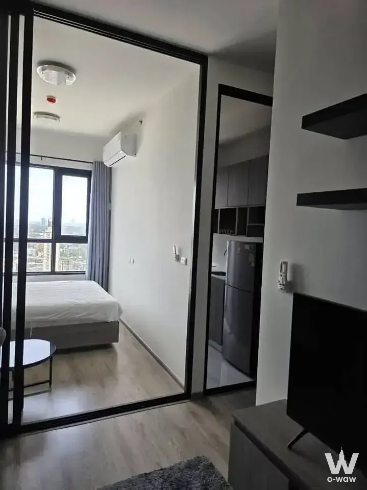 Open-plan studio with black floating shelves, TV area, and city skyline view through large window in KnightsBridge Prime