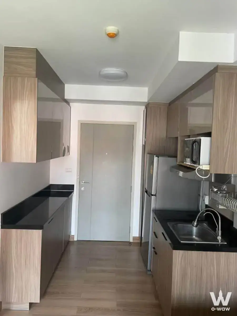 Galley kitchen in 1-bed condo at Chapter One The Campus Ladprao 1 with light wood cabinets and black countertops
