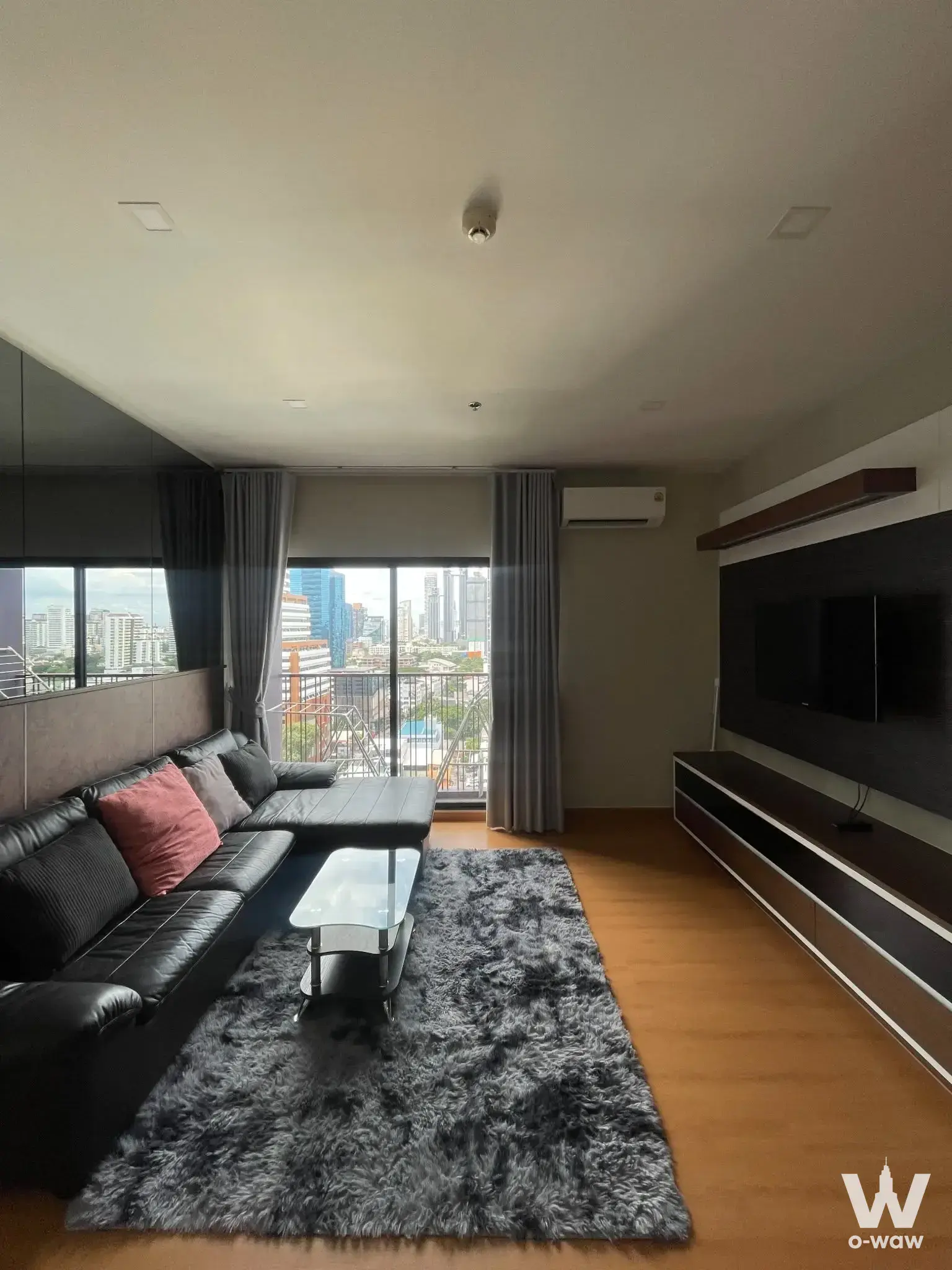 Living room in a 1-bed condo for rent at Noble Reveal with black leather sofa and city skyline view