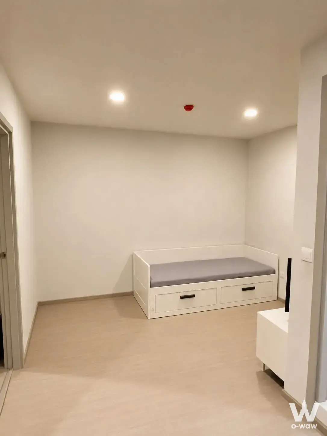 Empty bedroom with beige laminate flooring and white storage bed in Aspire Asoke-Ratchada condo