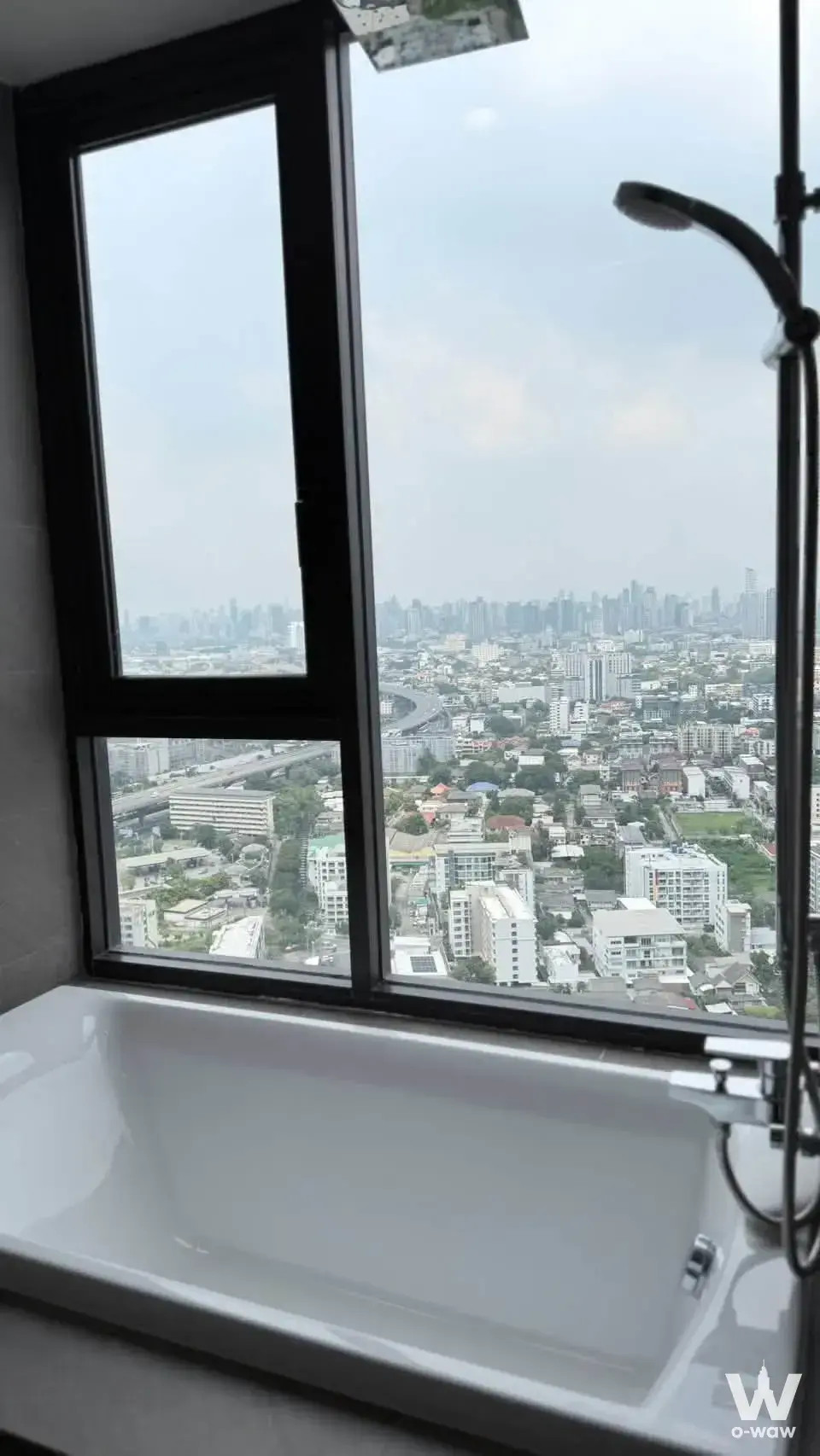 Modern bathroom with white bathtub and city skyline view in a 2-bed condo for rent at Skyrise Avenue Sukhumvit 64