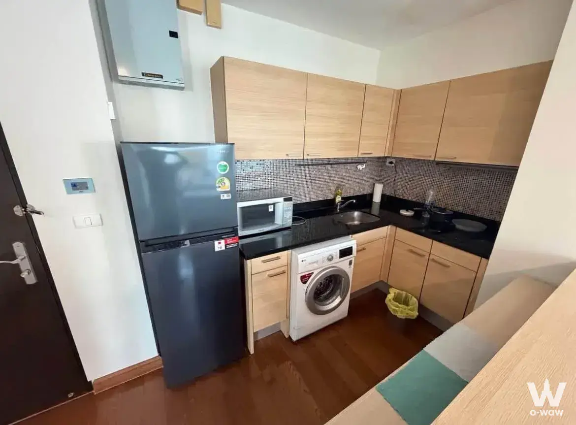 Modern L-shaped kitchen with oak cabinets and black countertops in 3-bed condo for rent at The Address Chidlom