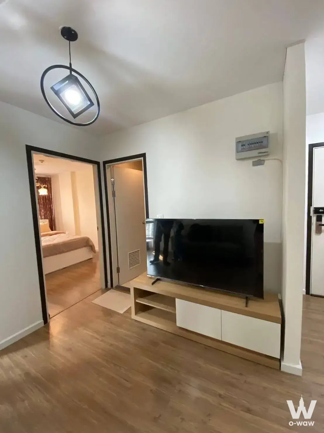 Minimalist condo living area featuring a TV console, pendant light, and open doorway to bedroom