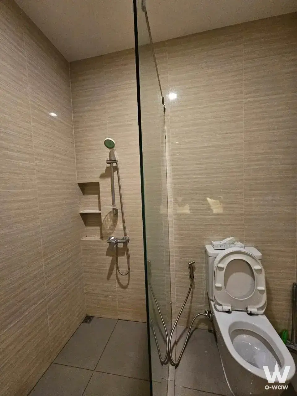 Modern M Jatujak condo bathroom with beige striated tiles, glass shower enclosure, and chrome fixtures
