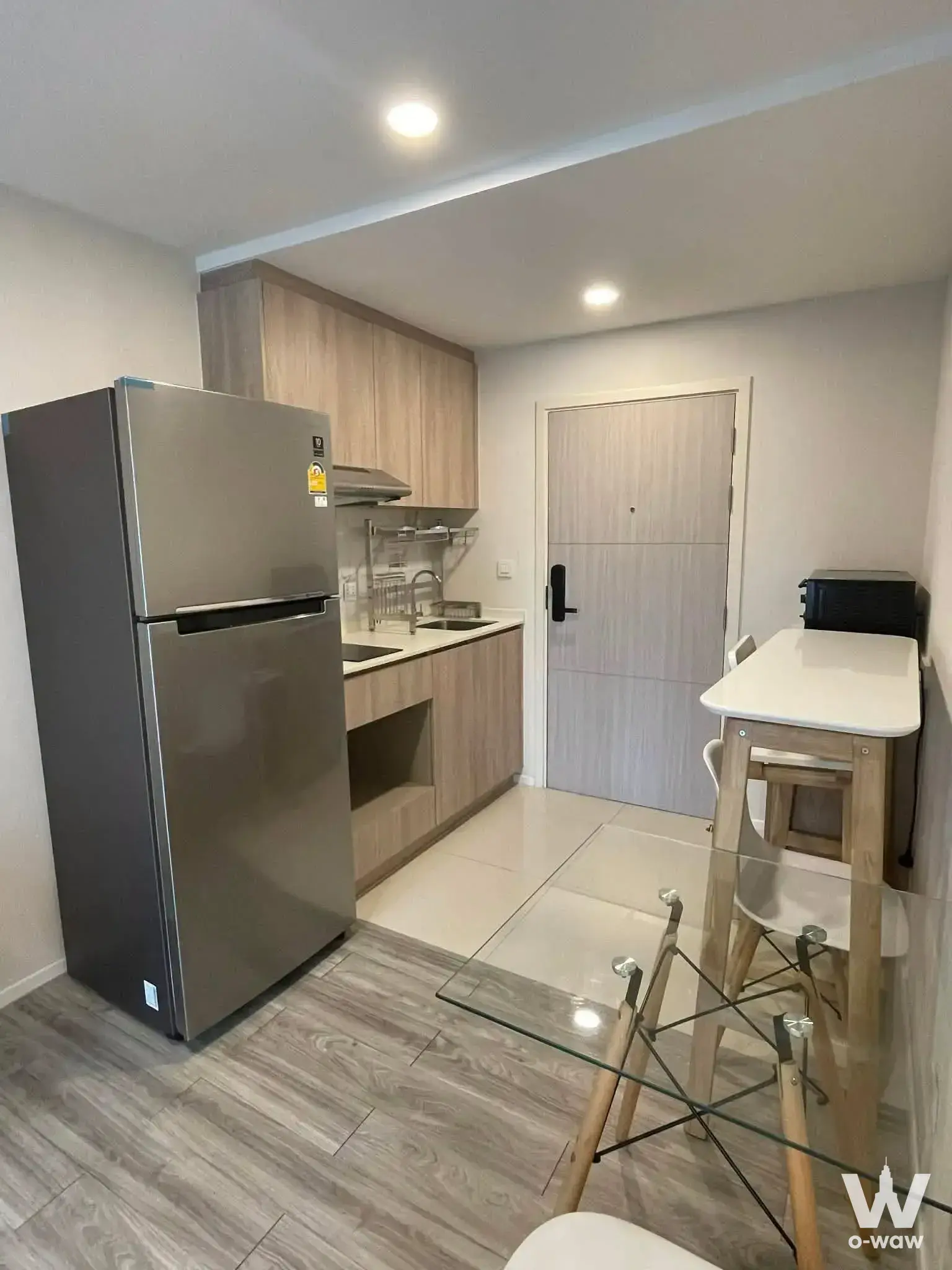Modern 1-bed condo kitchen in IKON Sukhumvit 77 with oak cabinets, white tiles, and stainless steel fridge