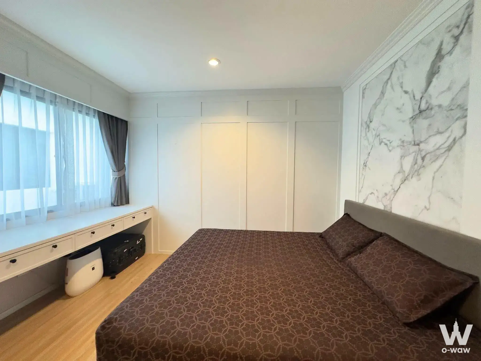 Modern bedroom in Nirvana Define Rama 9 townhouse with marble accent wall, built-in desk, and light wood flooring