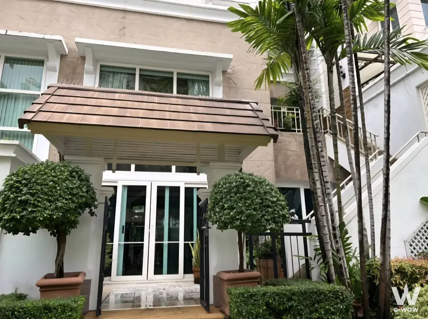 Entrance to Ladawan Na Chaopraya townhouse with teal doors and manicured topiary