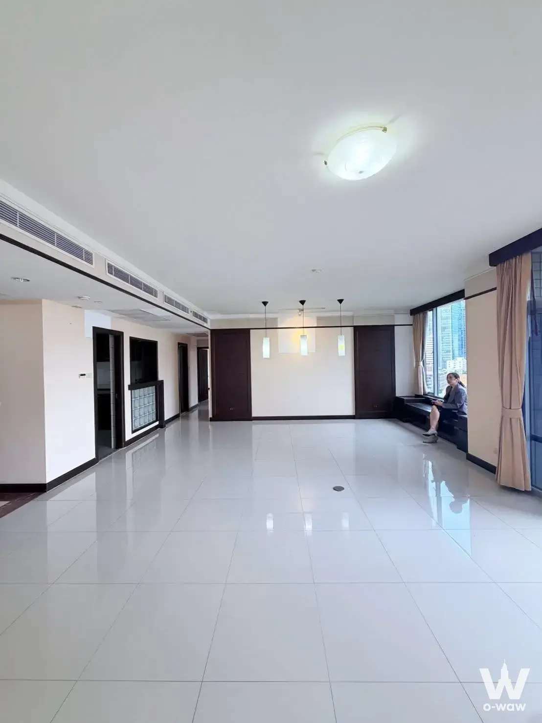 Empty living room in All Seasons Mansion with white tile floors, wood paneling, and woman on window seat