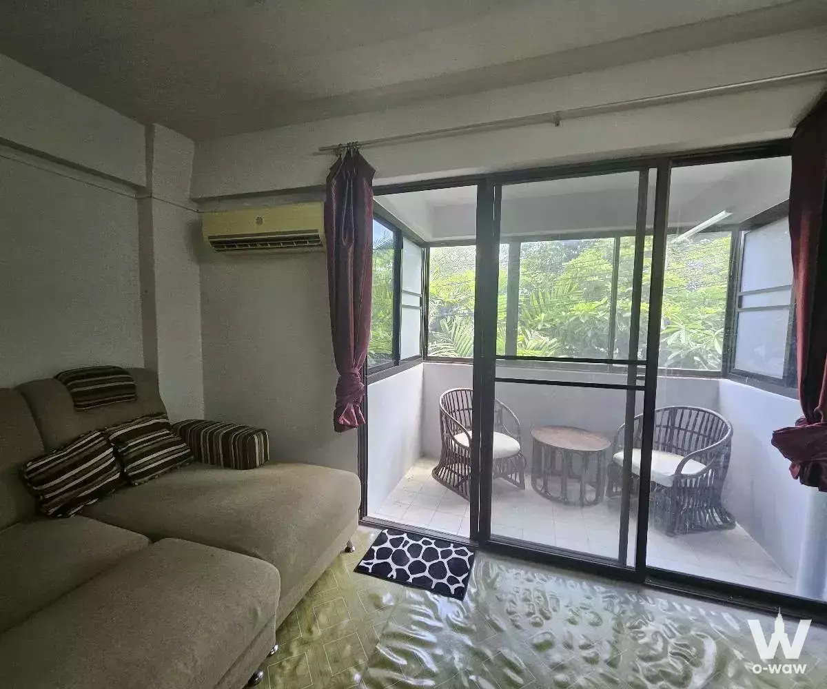 Living room with beige sectional sofa opening to enclosed balcony in 1-bed condo for sale at Victory View Condominium Bangkok