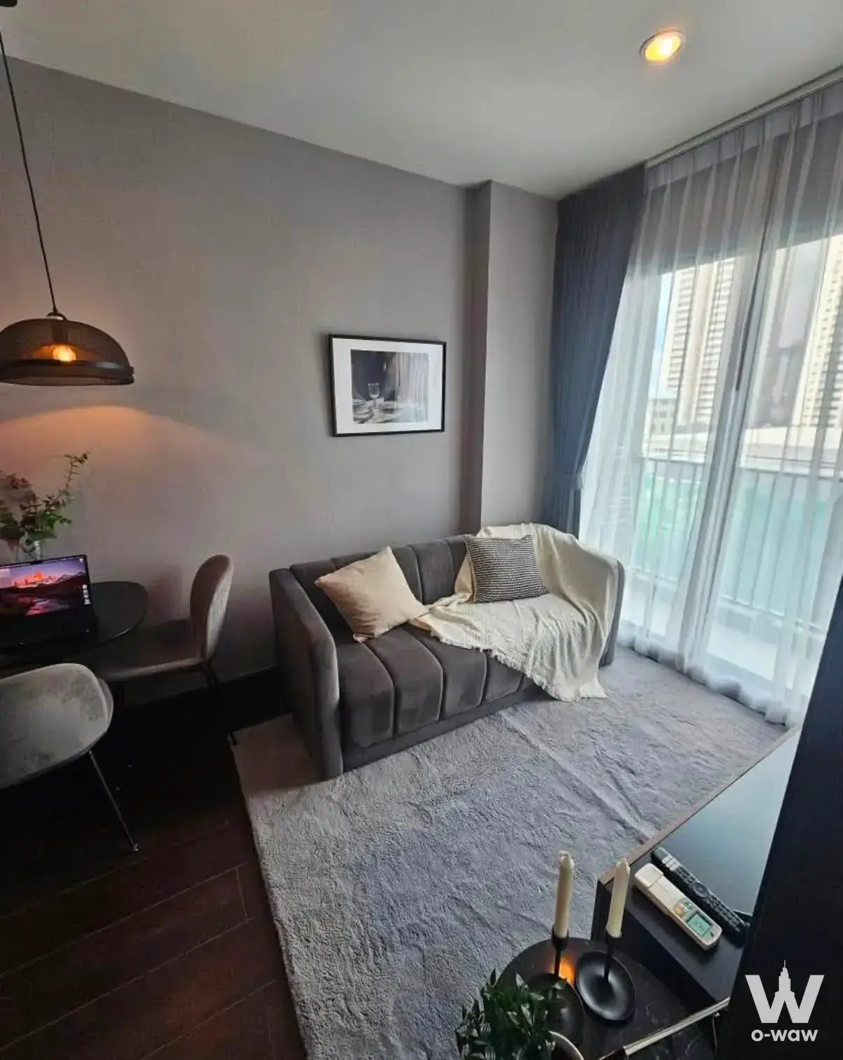 Modern living room in 1-bed C Ekkamai condo with grey sofa, wood floors, and city view from floor-to-ceiling windows