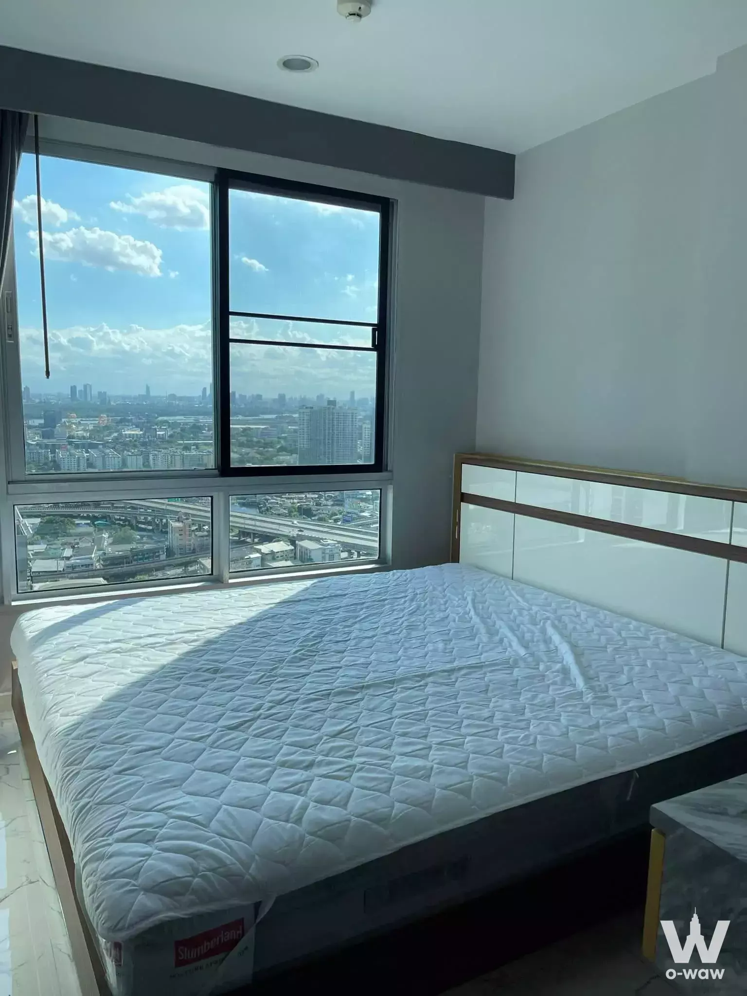 Bright bedroom in 1-bed THE BASE Sukhumvit 77 condo with queen bed, marble nightstand, and city views from floor-to-ceiling