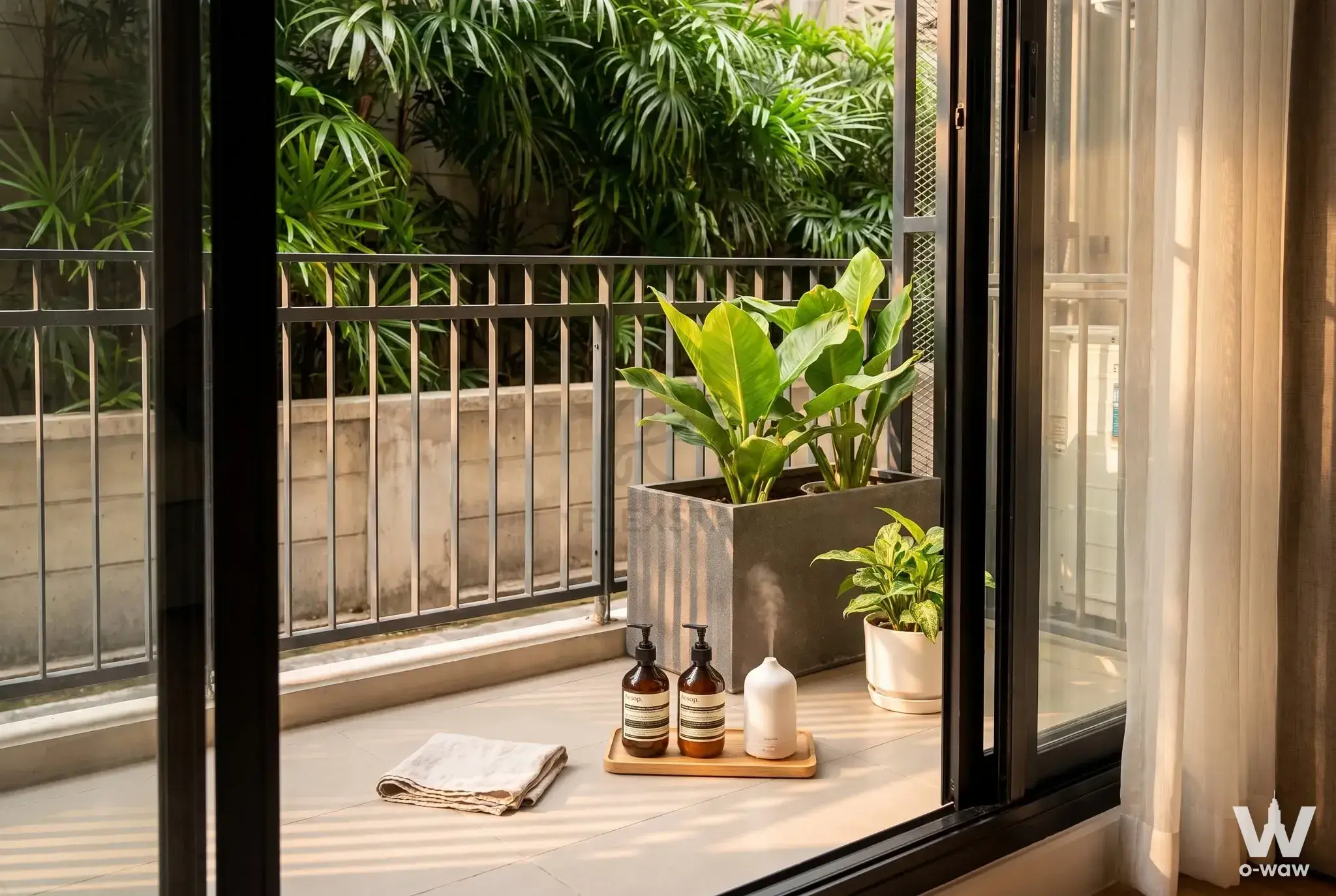 Balcony of a Blossom Condo Sathon unit with potted plants and dark metal railings facing dense tropical foliage