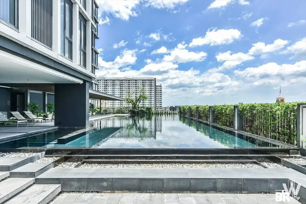 Rooftop infinity pool with blue water, lounge chairs, and city skyline views at QUINN Sukhumvit 101 luxury condo amenity