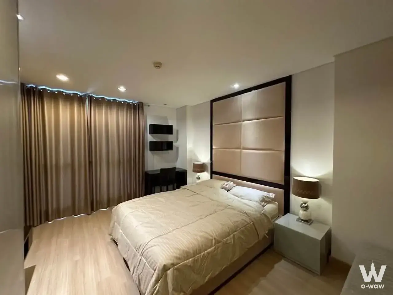 Modern condo bedroom with beige leather headboard, oak floors, and corner workspace