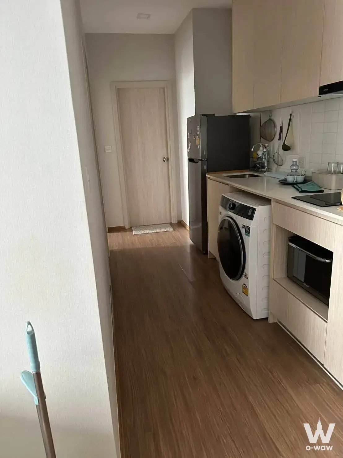 Modern condo kitchen with beige cabinets, stainless steel fridge, and integrated washing machine in narrow corridor