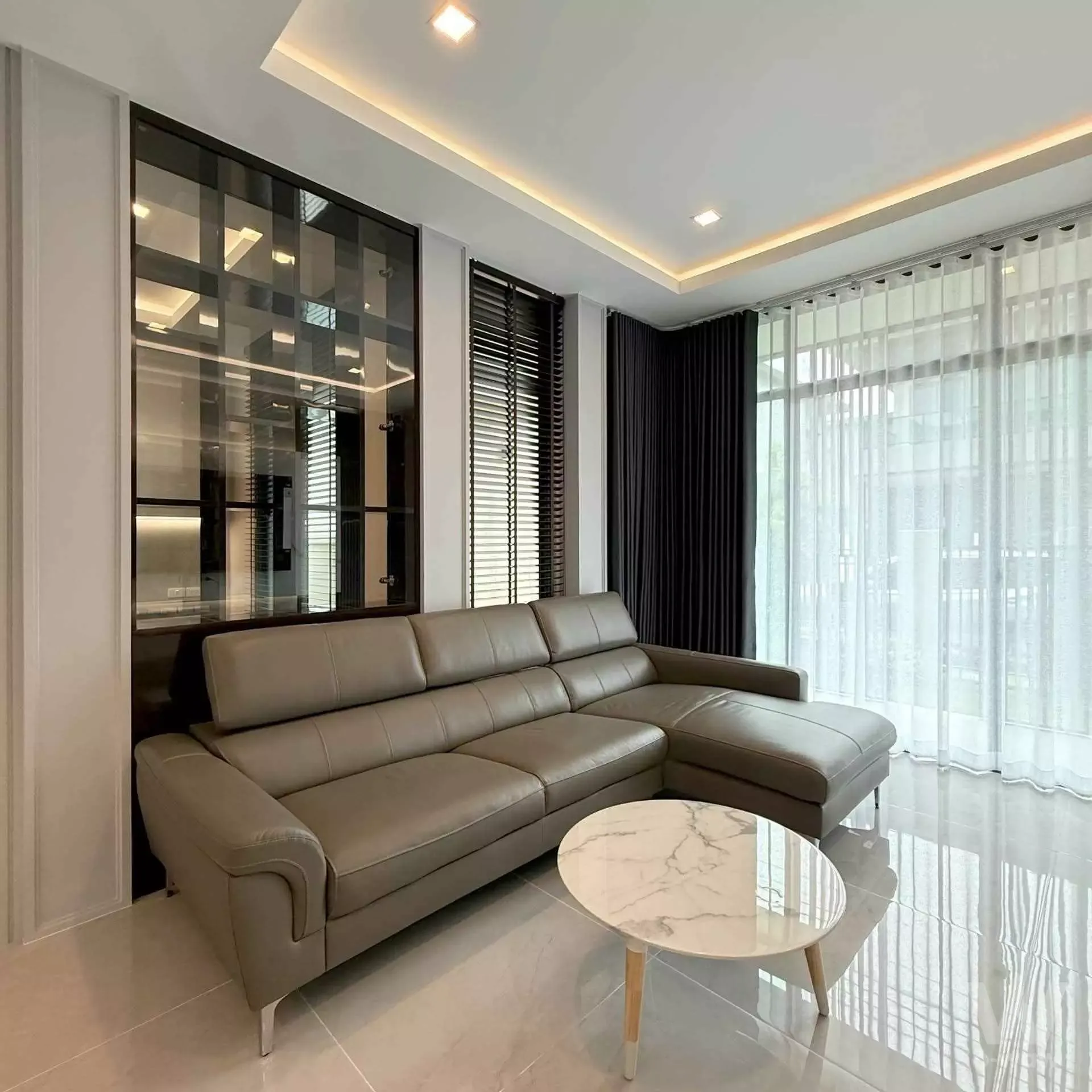 Modern living room with taupe leather sectional and marble coffee table in 3-bed condo for rent at Grand Bangkok Boulevard