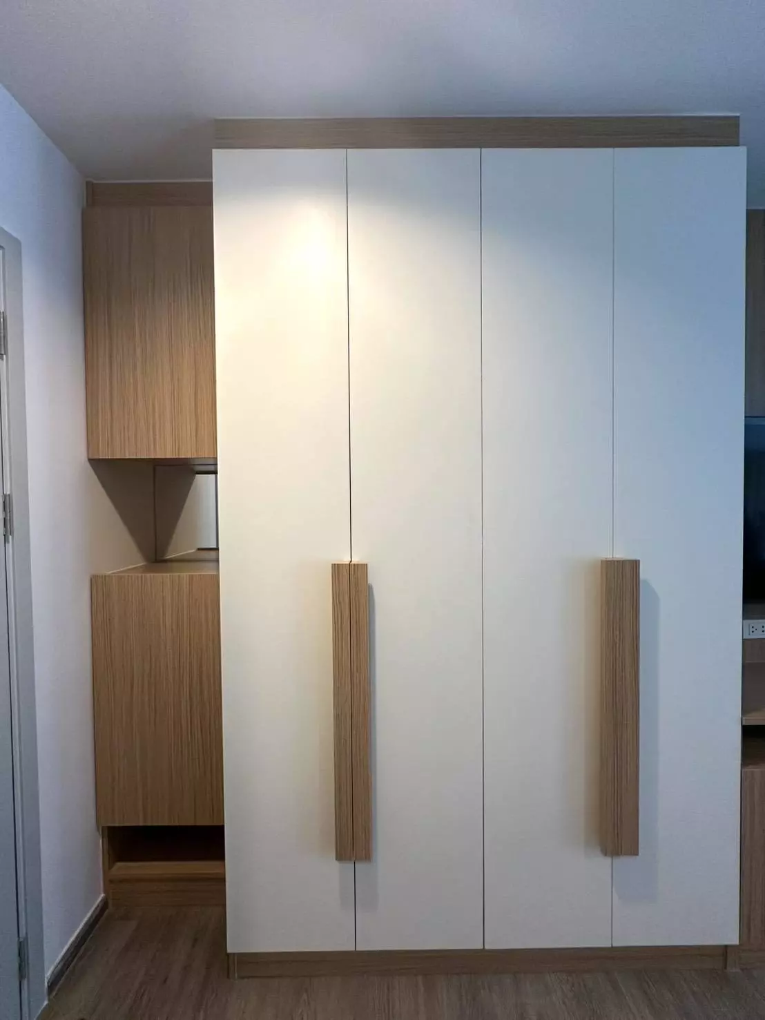 Modern bedroom with floor-to-ceiling white wardrobes and oak handles in 1-bed condo for rent at Regent Home Bangna