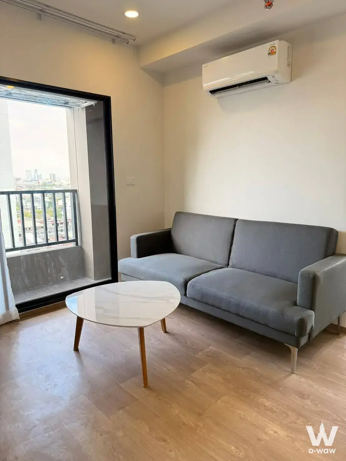 Living room with grey sofa and city skyline view in a So Origin Siriraj condo for rent