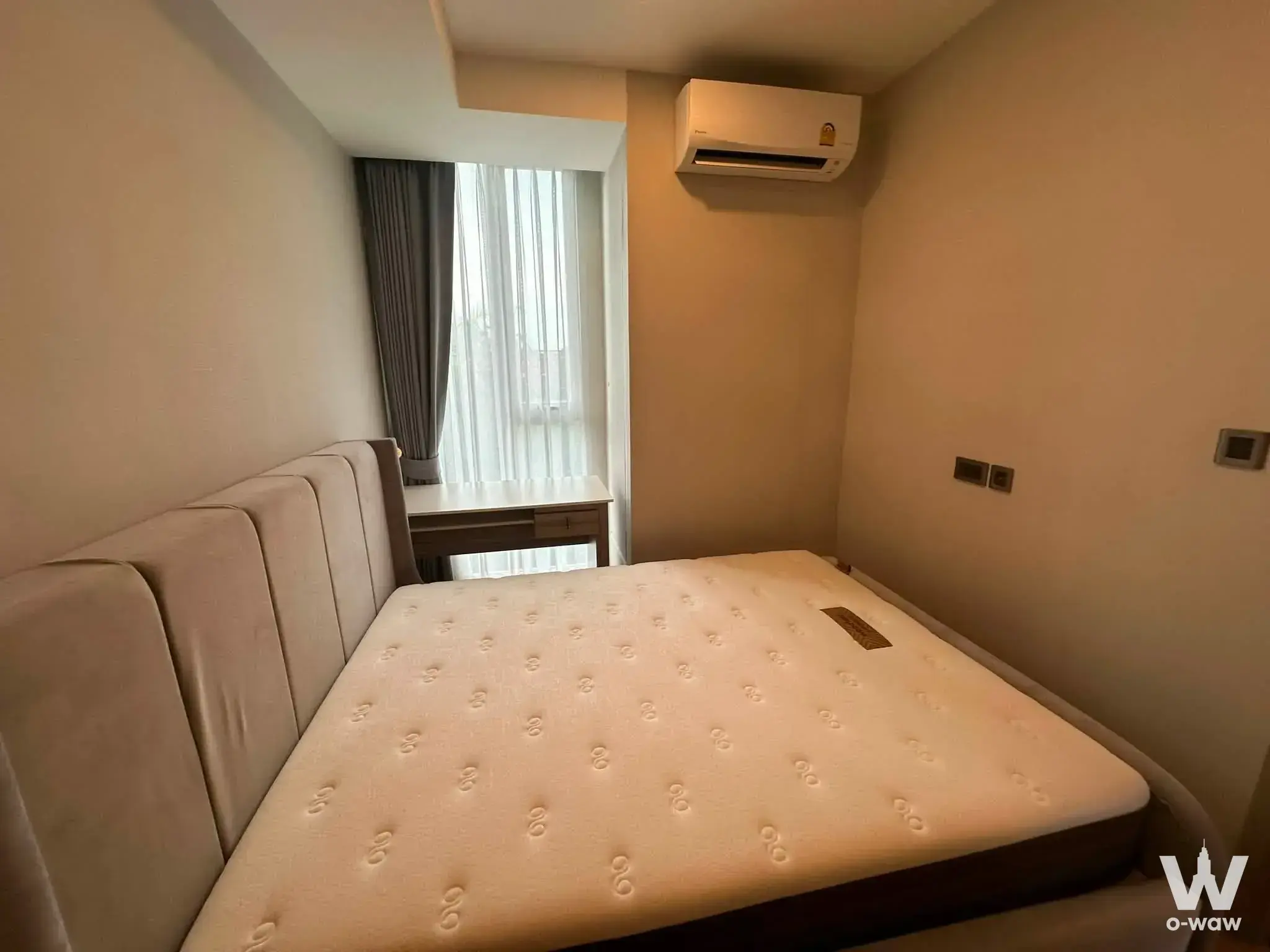 Minimalist bedroom in Chewathai Residence Thong Lo with a beige tufted bed and wooden desk
