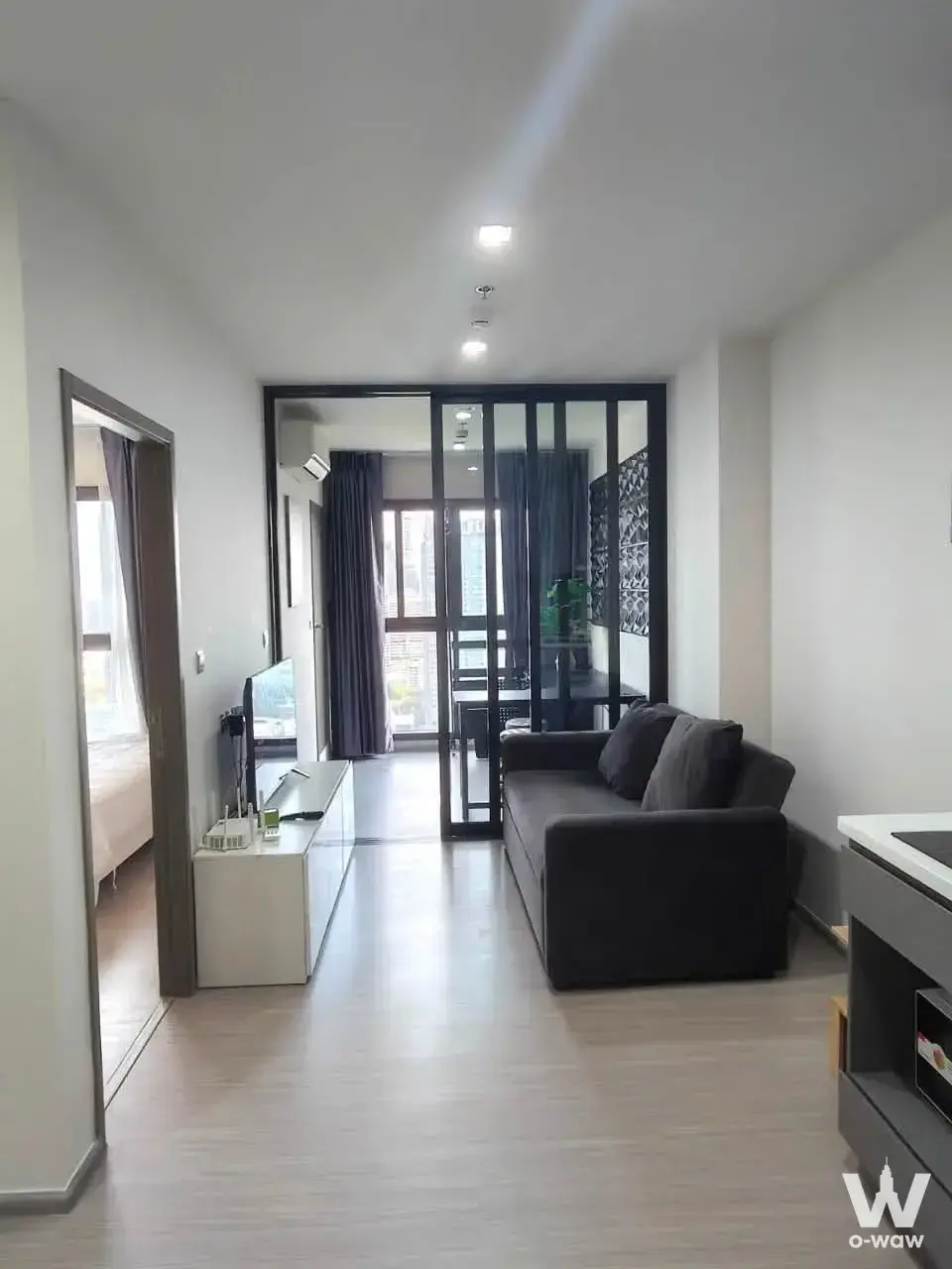 Modern condo living room with grey sofa, white TV console, light wood floors, and glass doors to balcony