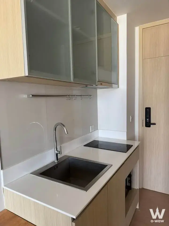 Modern kitchenette with light wood cabinets and induction cooktop in 1-bed condo for rent at MARU Ekkamai 2