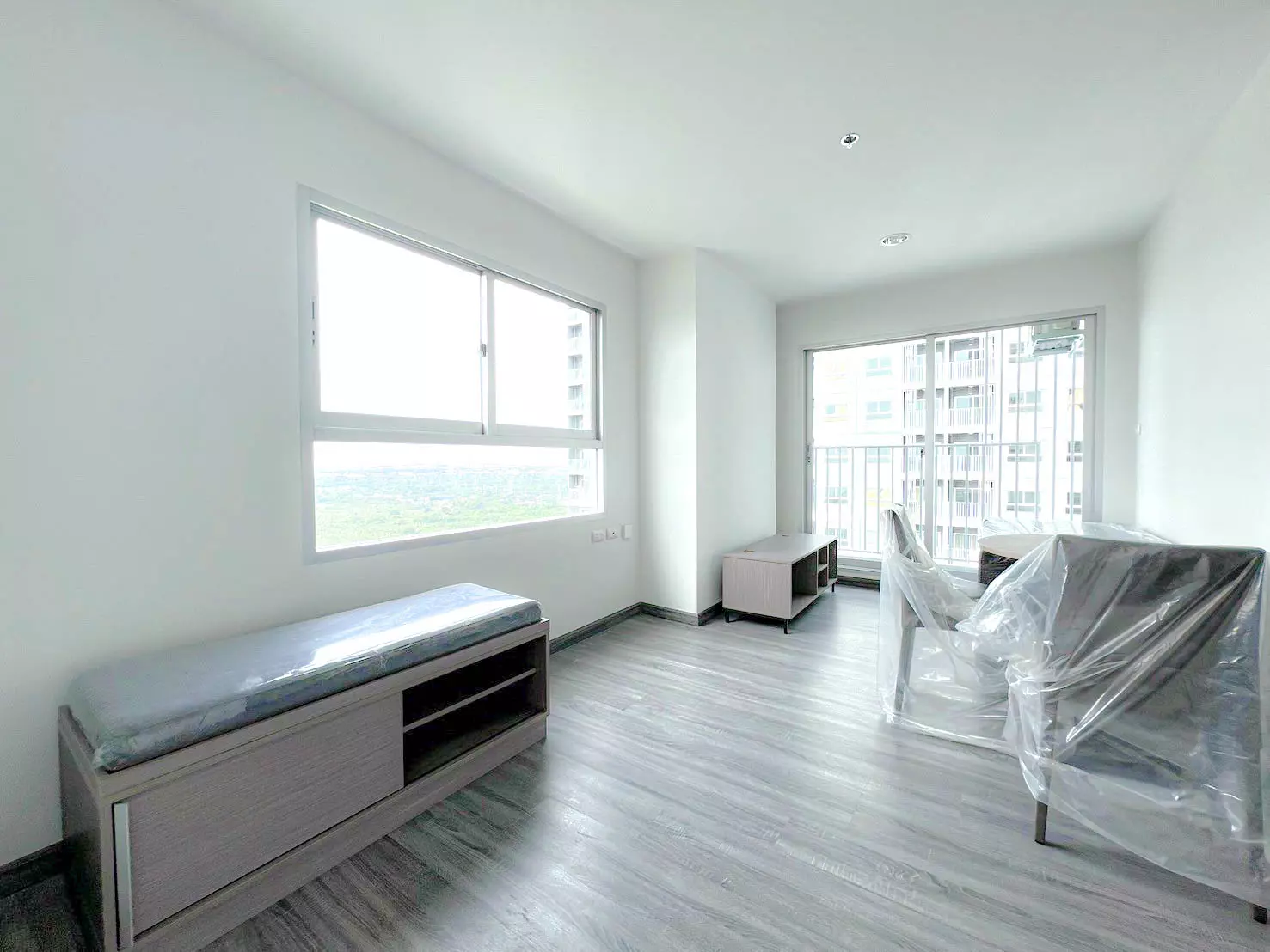 Bright living room with grey laminate floors and balcony access in 1-bed condo for sale at The Trust Condo @BTS Erawan