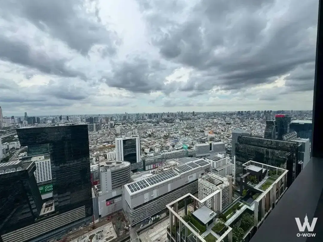High-floor balcony view of Bangkok skyline with glass towers and terraced greenery under dramatic overcast clouds