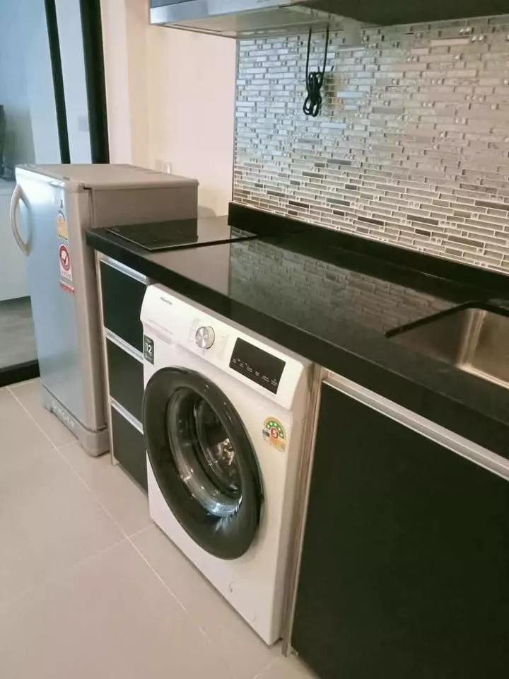 Compact kitchen in 1-bed condo for sale at Cybiq Ratchada 32 with glossy black countertop, induction cooktop, and integrated